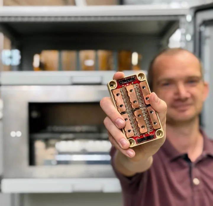 An HDX power module held up in the lab, with the HDPower DC/DC converter behind it.